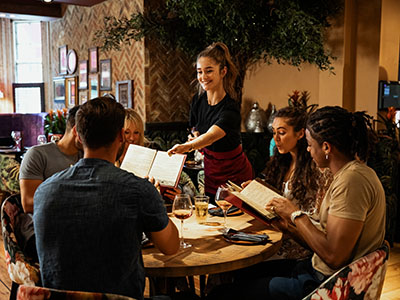 Kellnerin teilt Speisekarten an Tisch voll Gäste aus